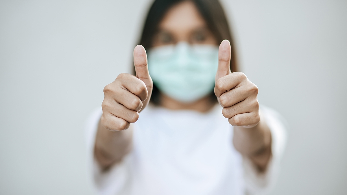 The women wear masks and mark them with their thumbs up.