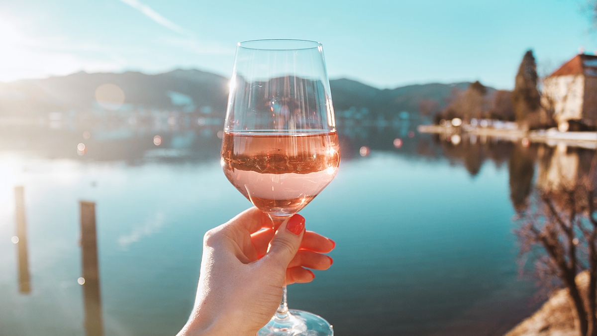 Female hand with glass of rose wine. Cozy pier on the coast of t
