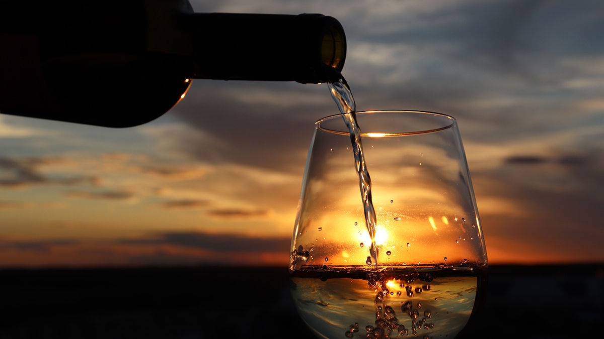 White wine pouring from a bottle into the glass on beautiful sun
