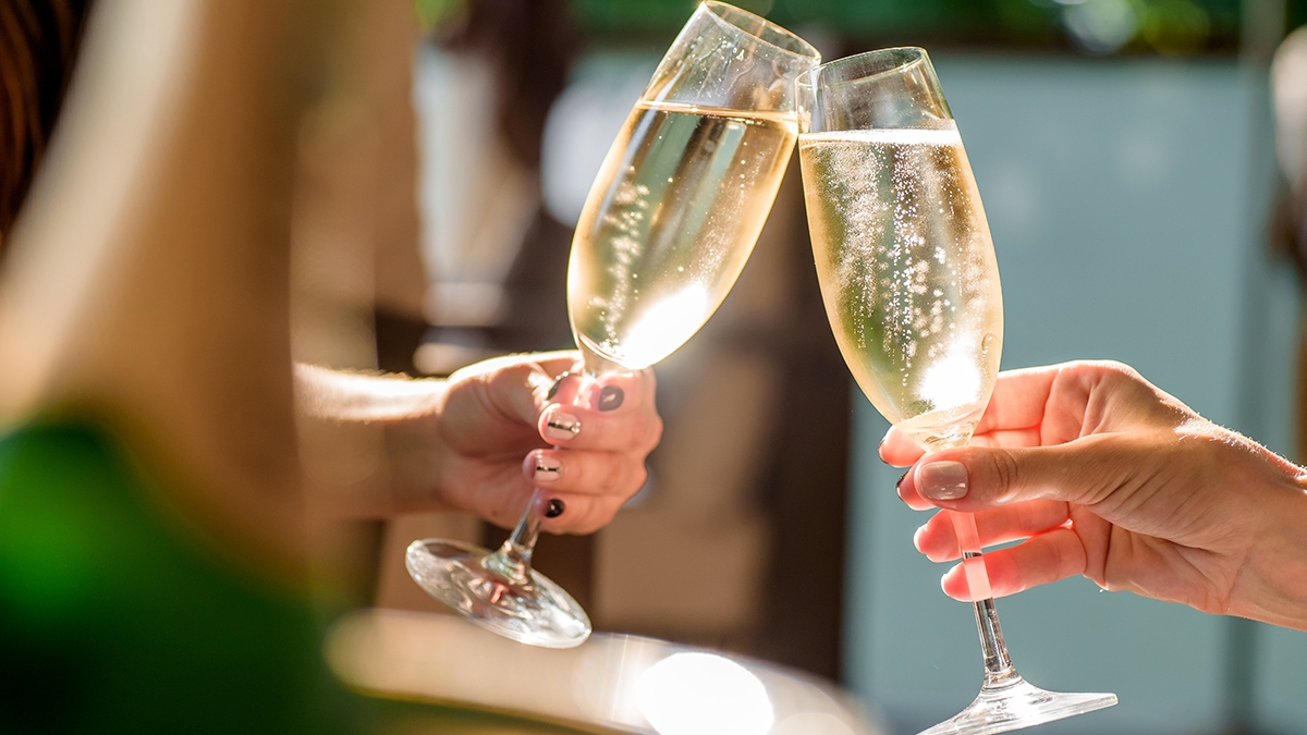 two girls clink glasses of champagne on a beautiful summer terrace. sparkling champagne glasses