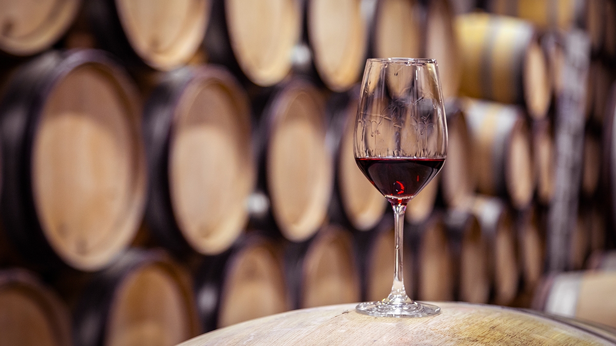Closeup glass with red wine on background wooden wine oak barrel