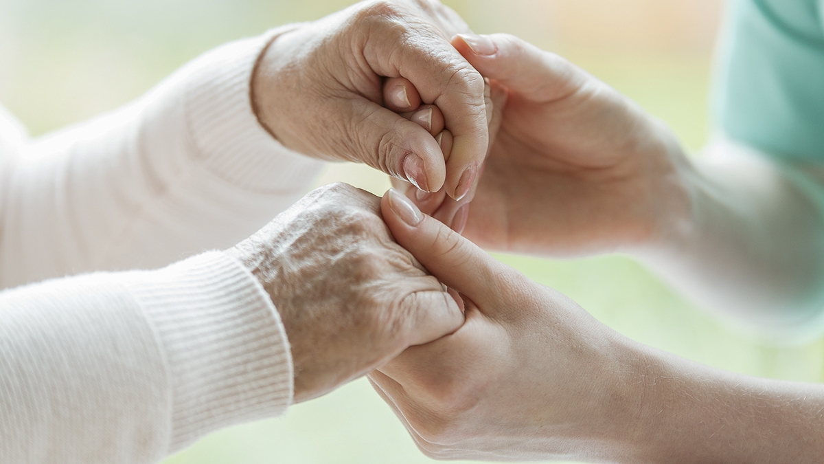 Closeup of the hands of a young woman holding hands of an elderl